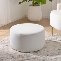 a white ottoman sitting on top of a rug in a living room next to a potted plant