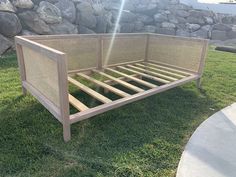 a wooden bed frame sitting on top of a green grass covered field next to a stone wall