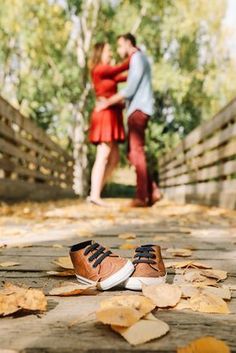 a man and woman standing on a bridge with leaves all over the ground in front of them