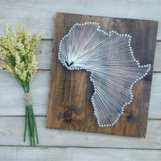 a string art piece next to some flowers on a wooden board with the shape of africa painted on it