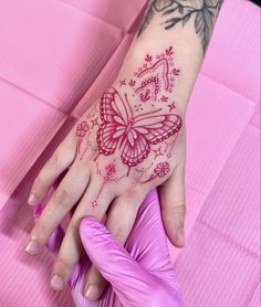 a woman's hand with a red butterfly tattoo on her left wrist and pink gloves