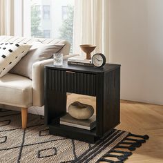 a living room with a couch, coffee table and clock on the end table in front of a window