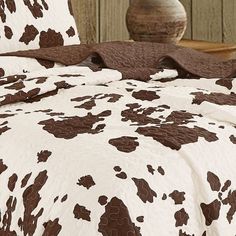 a cow print comforter set on a bed with pillows and pillow cases in front of a wooden wall