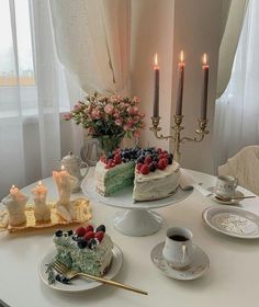 a table topped with two cakes covered in frosting next to cups and saucers