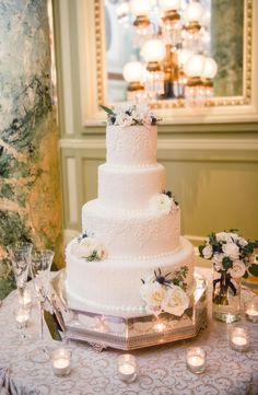 a white wedding cake sitting on top of a table next to candles and vases