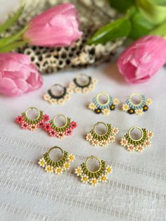 six pairs of beaded earrings sitting on top of a table next to pink flowers