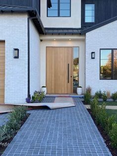 a white house with black trim and wood doors is shown in the evening light,