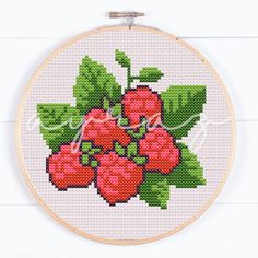 a cross stitch pattern with red flowers and green leaves on the hoop hanging on a white wall