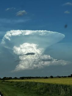 a large cloud is in the sky above a road and grass field on a sunny day