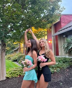 two beautiful young women standing next to each other in front of a house holding flowers