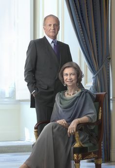 an older woman sitting on a chair next to a man in a suit and tie