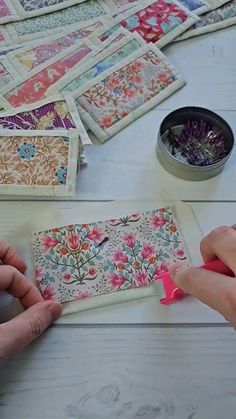 two hands are working on an intricately designed piece of fabric with pink crayons