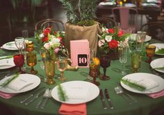 a green table topped with lots of plates and place settings next to a vase filled with flowers