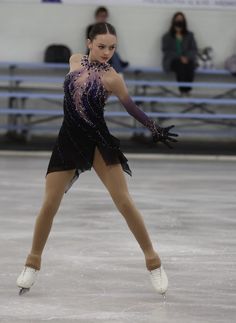 a female figure skating on an ice rink in a black leotard and purple dress