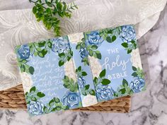 two cards with blue flowers on them sitting in a wicker basket next to a plant