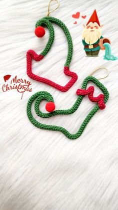 two green and red knitted christmas ornaments on a white furnishce with santa claus in the background