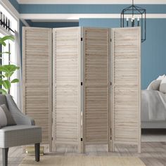 a room divider with shutters in front of a blue wall and white bed