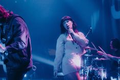 two people on stage with microphones in front of them and music instruments behind them