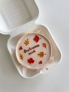 a cake in a white container with leaves on it and the words autumn written on it