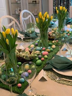 an easter table setting with flowers, eggs and greenery in vases on the table