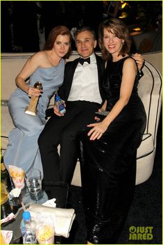 two women and a man sitting on a couch with drinks in their hands, posing for the camera