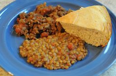 a blue plate topped with cornbreads, meat and baked beans next to a piece of bread