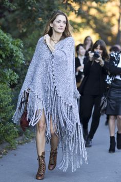 a woman is walking down the street in a fringed ponchy coat and boots