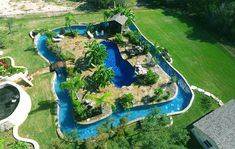 an aerial view of a pool surrounded by lush green grass and trees, with a house in the background