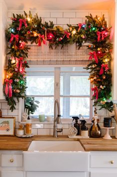 a kitchen decorated for christmas with wreaths and lights on the window sill above the sink