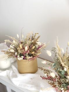 two vases filled with dried flowers on top of a white table next to a candle