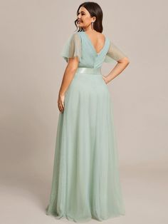 a woman in a long green dress is looking back at the camera and she has her hands on her hips