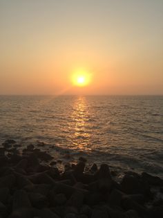 the sun is setting over the ocean with rocks on the shore and in the foreground