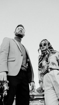 a man and woman standing next to each other in front of a car with sunglasses on