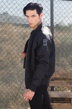 a young man standing next to a fence with his hand in his pocket and looking at the camera