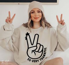 a woman sitting on top of a bed wearing a white sweatshirt with the peace sign