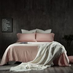 a bed with pink linens and pillows in a dark room, next to a potted plant