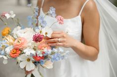 a woman in a wedding dress holding a bridal bouquet with white, pink and blue flowers