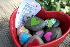 a red bowl filled with rocks covered in colorful heart shaped magnets and paper on top of a wooden table