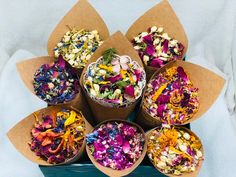 a basket filled with lots of different types of flowers in paper cones on top of a white blanket