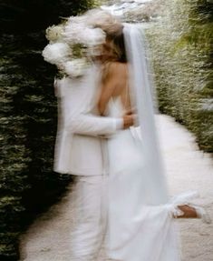 a bride and groom are hugging in front of some bushes with white flowers on their head