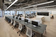 an empty office with desks and computers on the long table in front of large windows