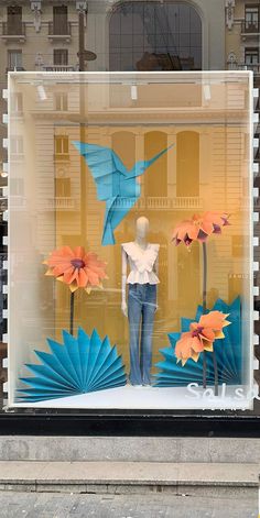 a window display with paper flowers and birds in the front, behind which is a mannequin's head