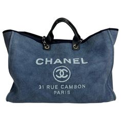 Chanel Denim Blue XL Deauville Tote - Circa 2012 This very popular Chanel tote is made from a denim blue canvas with white Lettering/Logo. The design of the tote bag has an open top that has an interior large snap, rolled leather top handles, and a detachable shoulder strap woven with chain links in silver-tone hardware. Being the XL style this tote has an Interior that is very spacious with a fabric lining. The interior has multiple pockets, there is a large 10" main pocket with a zipper closur Tote Chanel, 31 Rue Cambon, Tas Denim, Chanel Denim, Chanel Canvas, Chanel Lover, Gucci Soho, Chanel Brand, Michael Kors Selma