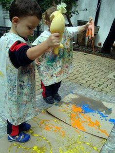 a little boy holding a stuffed animal on top of a cardboard box covered in paint