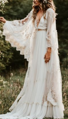 a woman wearing a white wedding dress in the middle of a field with trees behind her