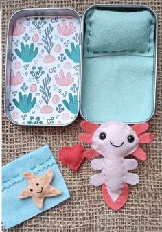 an open tin with some felt animals in it and two other items next to it