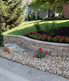 a stone wall and flower bed in front of a house