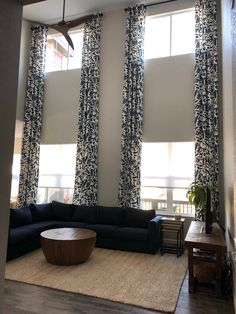 the living room is decorated with blue and white curtains, black couches, and a large round coffee table