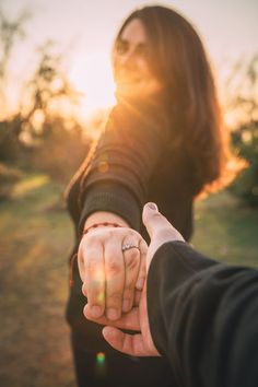 a man and woman holding hands with the sun setting in the back ground behind them