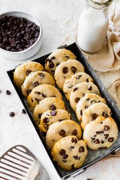 chocolate chip cookies in a baking pan next to a glass of milk and a spatula